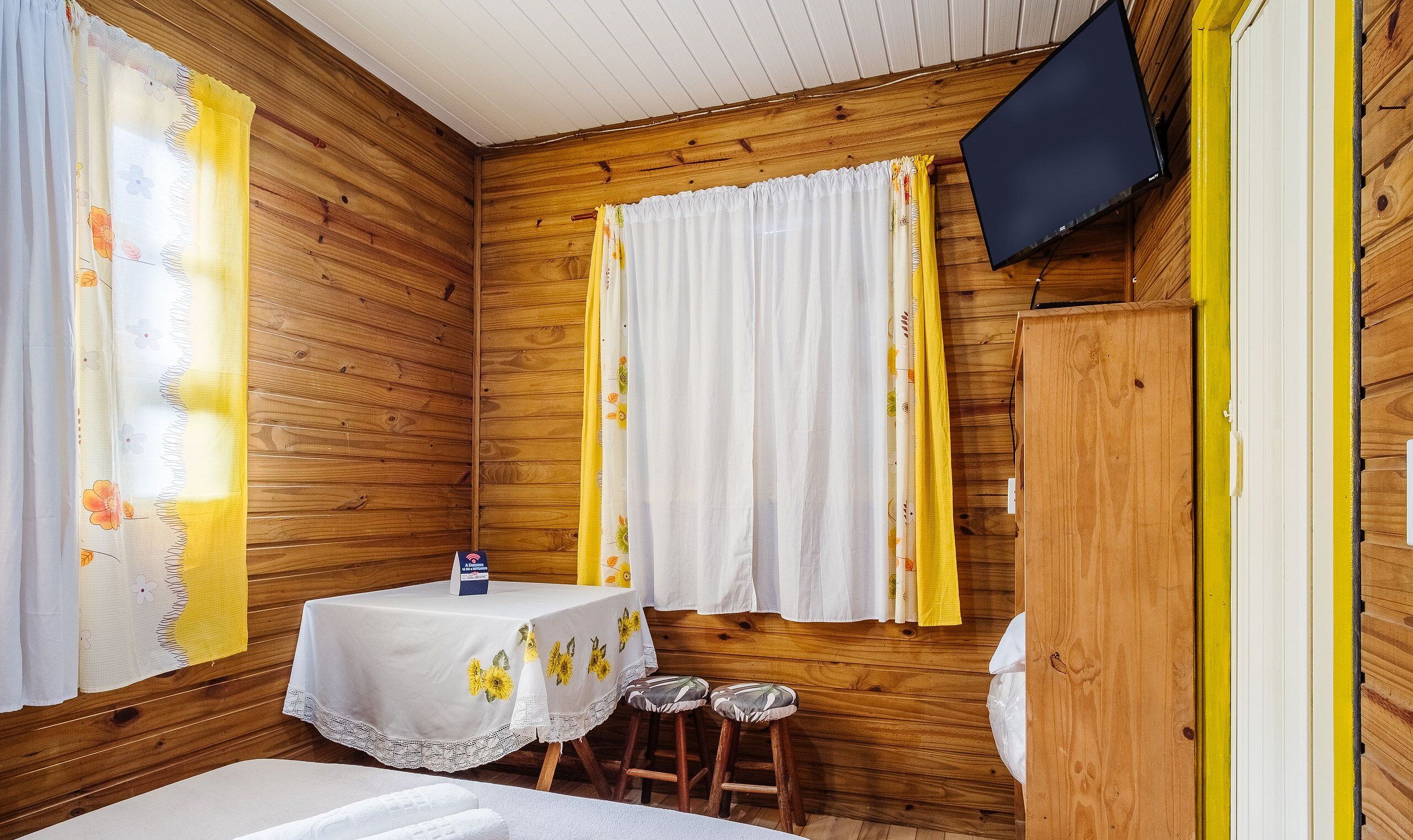 A wooden room with a bed, a table, and a TV mounted on the wall.