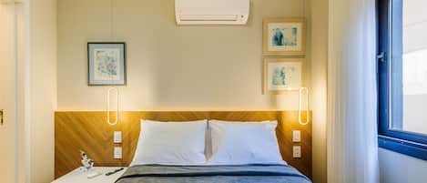 Une chambre d’hôtel comprenant un lit, des tables de chevet, une commode, un appareil de climatisation et des œuvres d’art encadrées accrochées au mur.