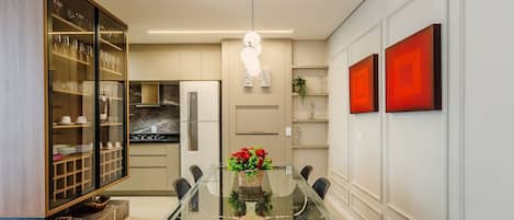 A modern kitchen with a glass dining table, stainless steel appliances, and red artwork on the wall.