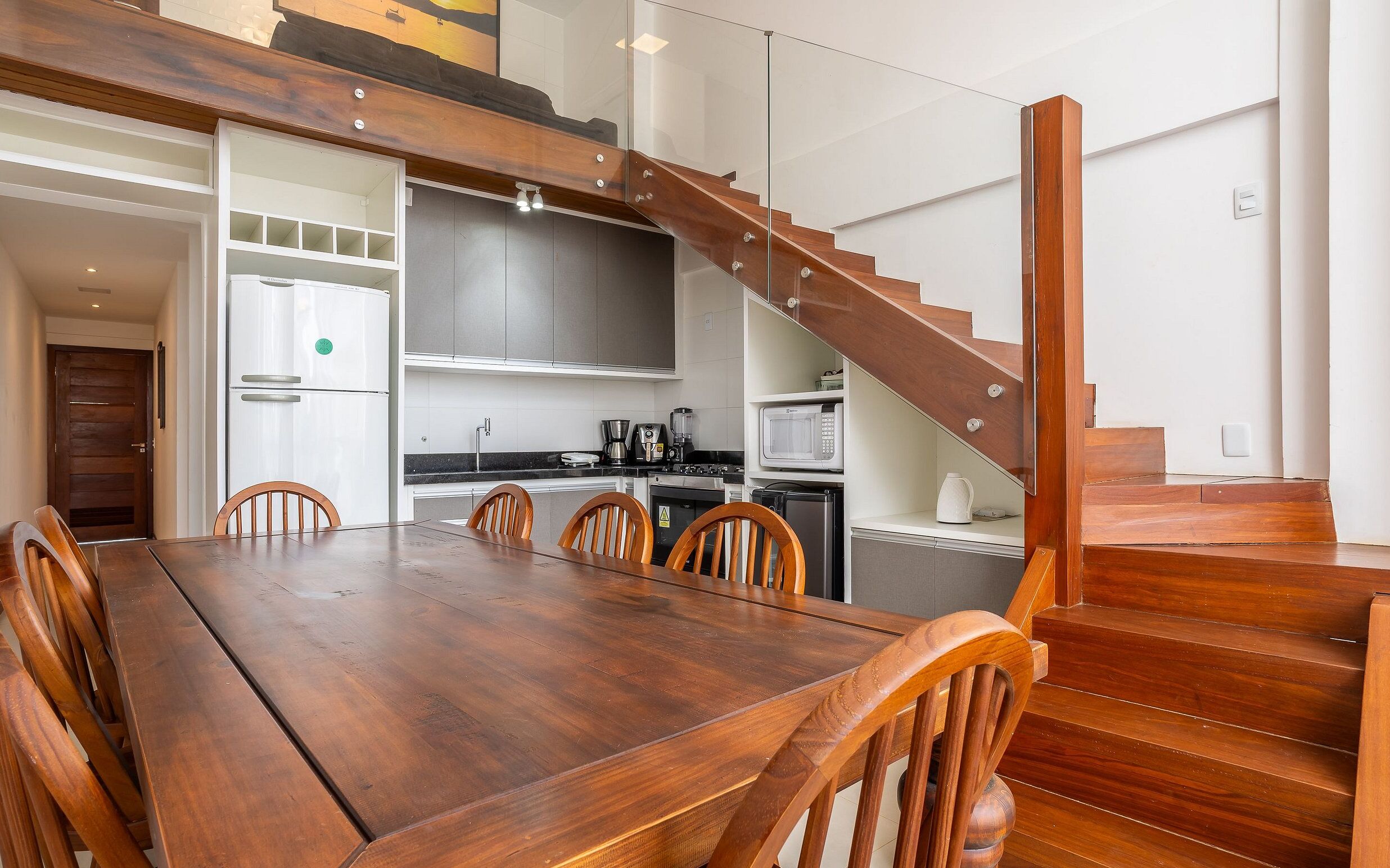 Una cocina moderna con una escalera de madera, un comedor con una mesa grande y sillas, y vista del espacio de estar contiguo.