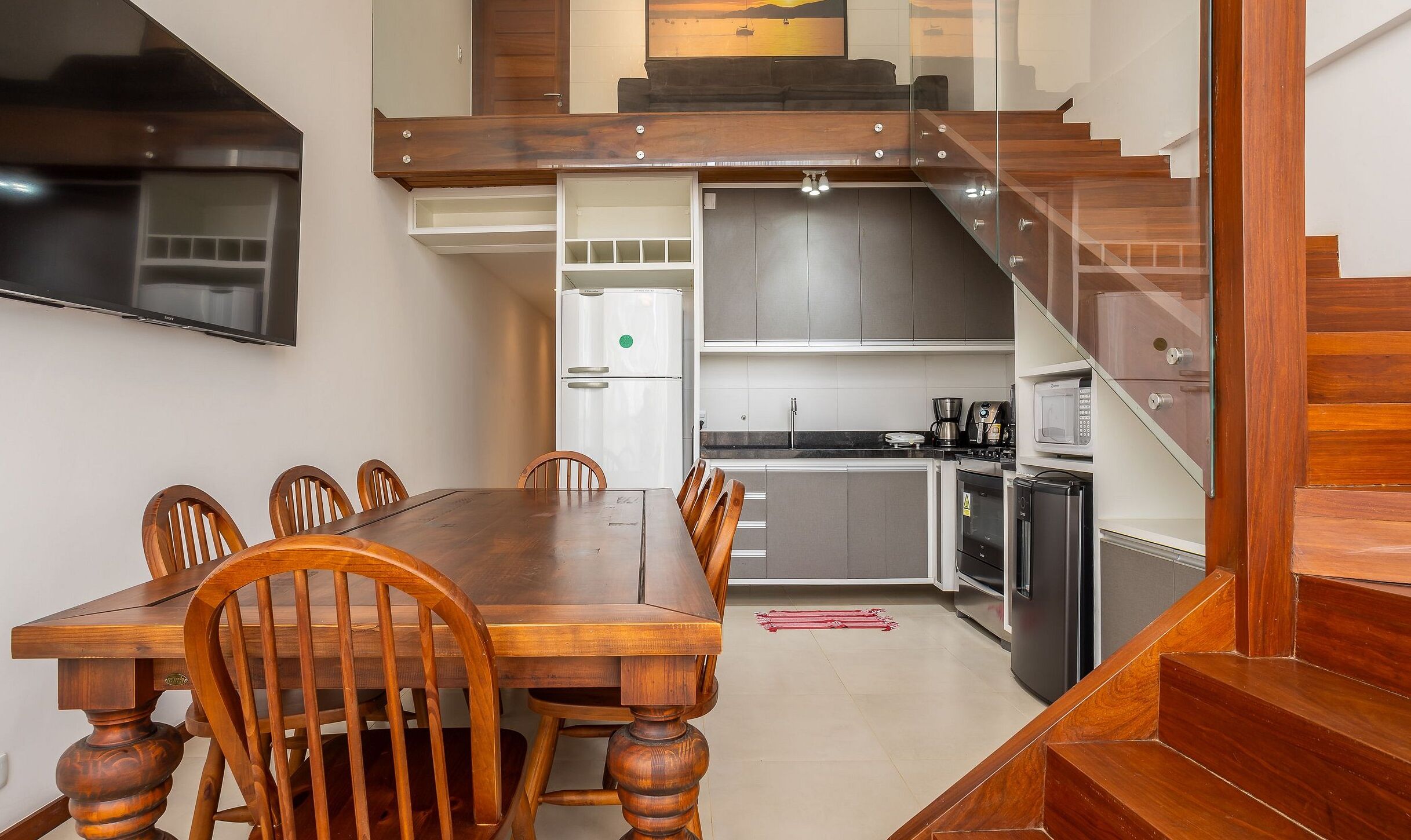 Un comedor con mesa y sillas de madera, una cocina con electrodomésticos modernos y una escalera que sube a un nivel superior.