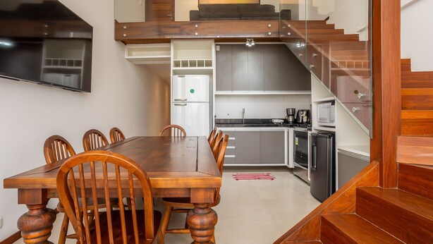 A dining area with a wooden table and chairs, a kitchen with modern appliances, and a staircase leading to an upper level. - Two-story Apt 200m From Barra Grande Beach Cpr0207 (Maraú)