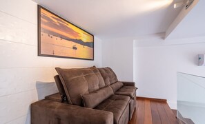 Ein modernes Wohnzimmer mit einem braunen Sofa, einem großen Sonnenuntergangsbild in einem Rahmen und einer Wand mit weißen Fliesen.