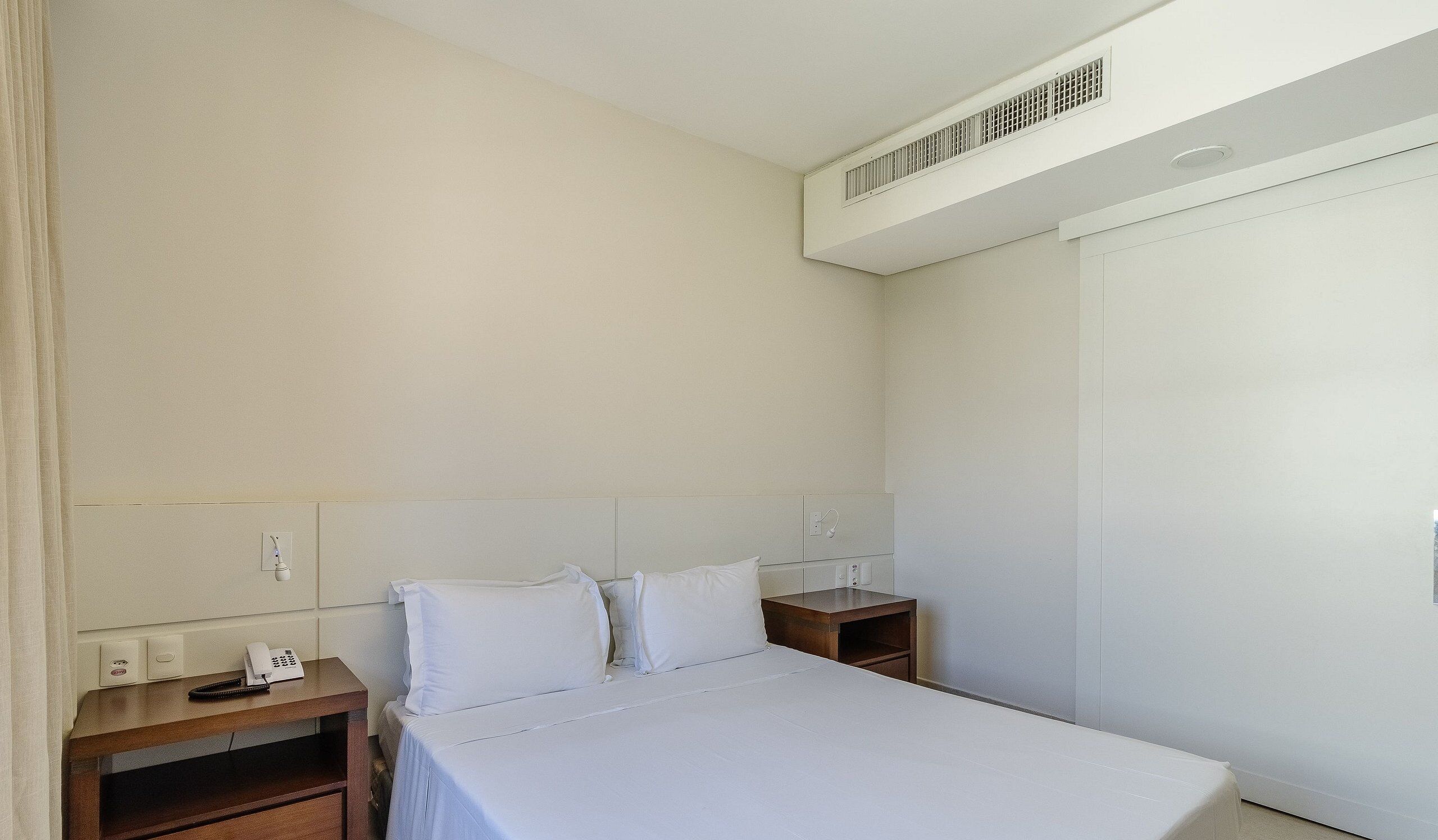 Une chambre d’hôtel comprenant un lit, des tables de chevet, un téléphone et une armoire.