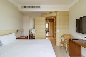 A hotel room with a bed, a desk, a television, and a wardrobe. - Sea View Apartment in Luxury Resort - Jbv207 (Florianópolis)