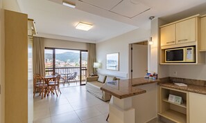 Een hotelkamer met balkon, eethoek, kitchenette en een bed.