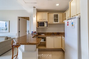 A compact kitchen with a microwave, refrigerator, and wooden cabinets. - Sea View Apartment in Luxury Resort - Jbv207 (Florianópolis)