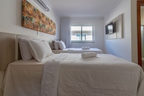 Ein Hotelzimmer mit zwei Betten, einem großen Fenster, einem Flachbildfernseher und einem tropischen Kunstwerk an der Wand.