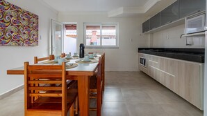 A modern kitchen with wooden cabinets, a black countertop, and a dining area with a wooden table and chairs. - House in Condo With Pool Near the Beach Mgi025 (Porto Seguro)