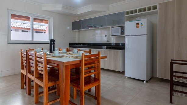 A modern kitchen with a dining area, white cabinetry, a microwave, and a refrigerator. - House in Condo With Pool Near the Beach Mgi025 (Porto Seguro)