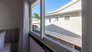 A bedroom with a window, a bed, and a view of neighboring buildings. - House in Condo With Pool Near the Beach Mgi025 (Porto Seguro)