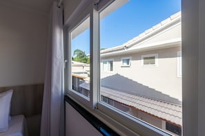 Ein Schlafzimmer mit Fenster, Bett und Blick auf umliegende Gebäude.