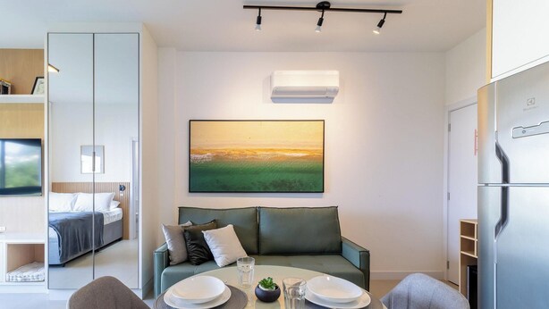 A modern living room with a sofa, a dining table set with plates and glasses, a painting on the wall, and a refrigerator. - Modern Studio in Condominium With sea View Vpd0605 (Florianópolis)