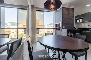Un comedor moderno con una gran mesa redonda y sillas, una pared negra con horno empotrado y ventanas amplias que ofrecen vistas a la ciudad.