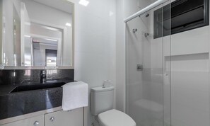 Un baño moderno con lavamanos de encimera negro, inodoro y cabina de ducha con paredes de vidrio.