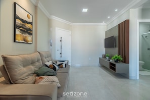 Uma sala de estar moderna com um sofá bege, televisão na parede e design minimalista.