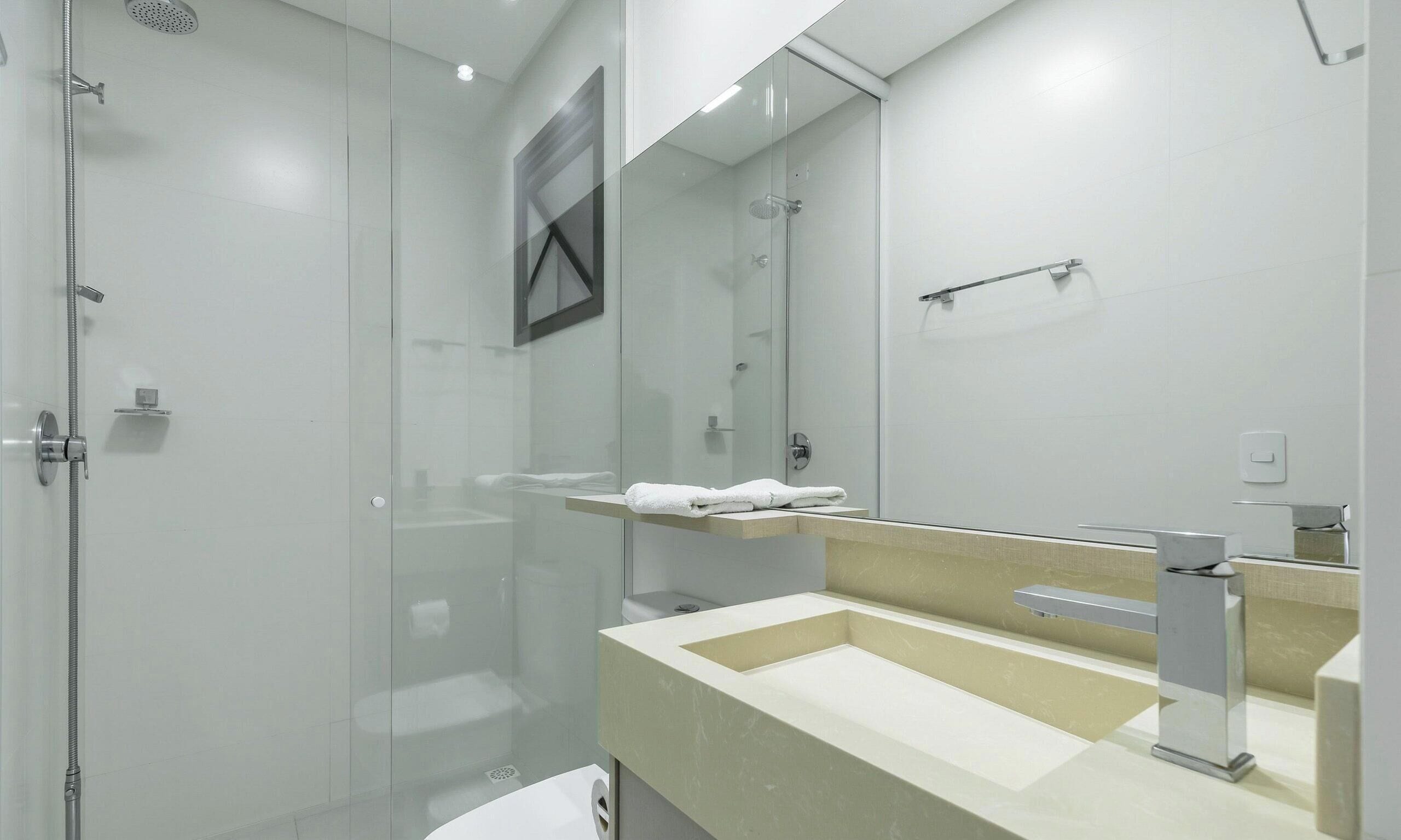 Un baño moderno con ducha de vidrio, lavamanos con espejo y un perchero para toallas.
