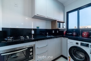 A modern kitchen with a built-in oven, a washing machine, and a large window. - 2B Apt w/ Barbecue by the sea Uml0104 (Bombinhas)