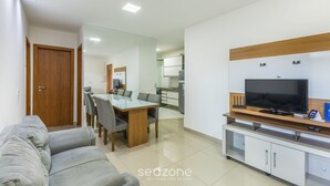 A modern living room with a sofa, dining table, TV, and kitchen area. - 2-bedro ap in Cond W/pool, 850 m the Beach Vgt0004 (Ilhéus)