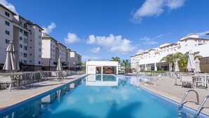 A swimming pool with lounge chairs and umbrellas, surrounded by multi-story buildings with balconies. - 2-bedro ap in Cond W/pool, 850 m the Beach Vgt0004 (Ilhéus)