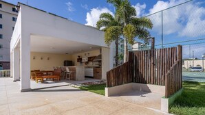 A covered outdoor area with a dining table and chairs, a kitchen area, and a fenced garden. - 2-bedro ap in Cond W/pool, 850 m the Beach Vgt0004 (Ilhéus)