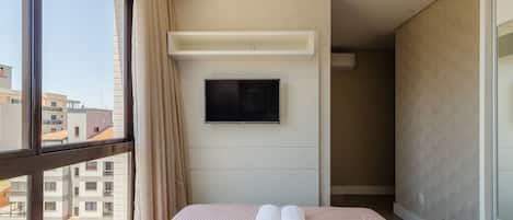 A hotel room with a bed, a flat-screen TV mounted on the wall, and a window with curtains.