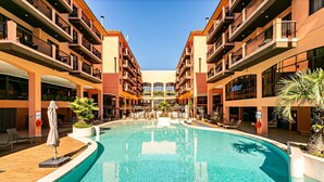 Um hotel com piscina central, várias varandas e áreas de estar ao ar livre.