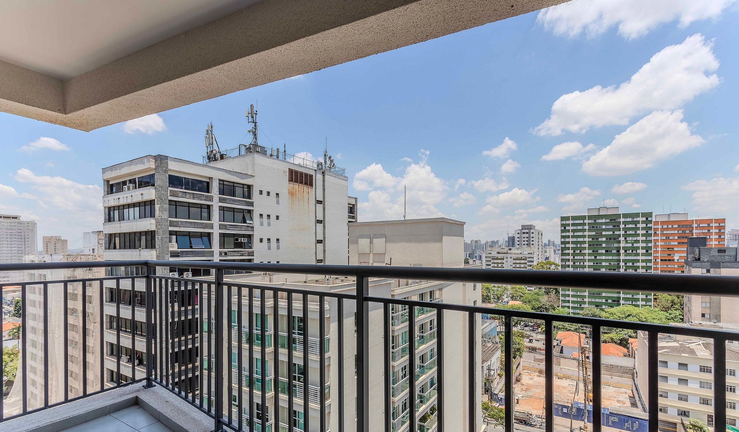 A balcony with a view of a cityscape, featuring multi-story buildings and a clear sky.
