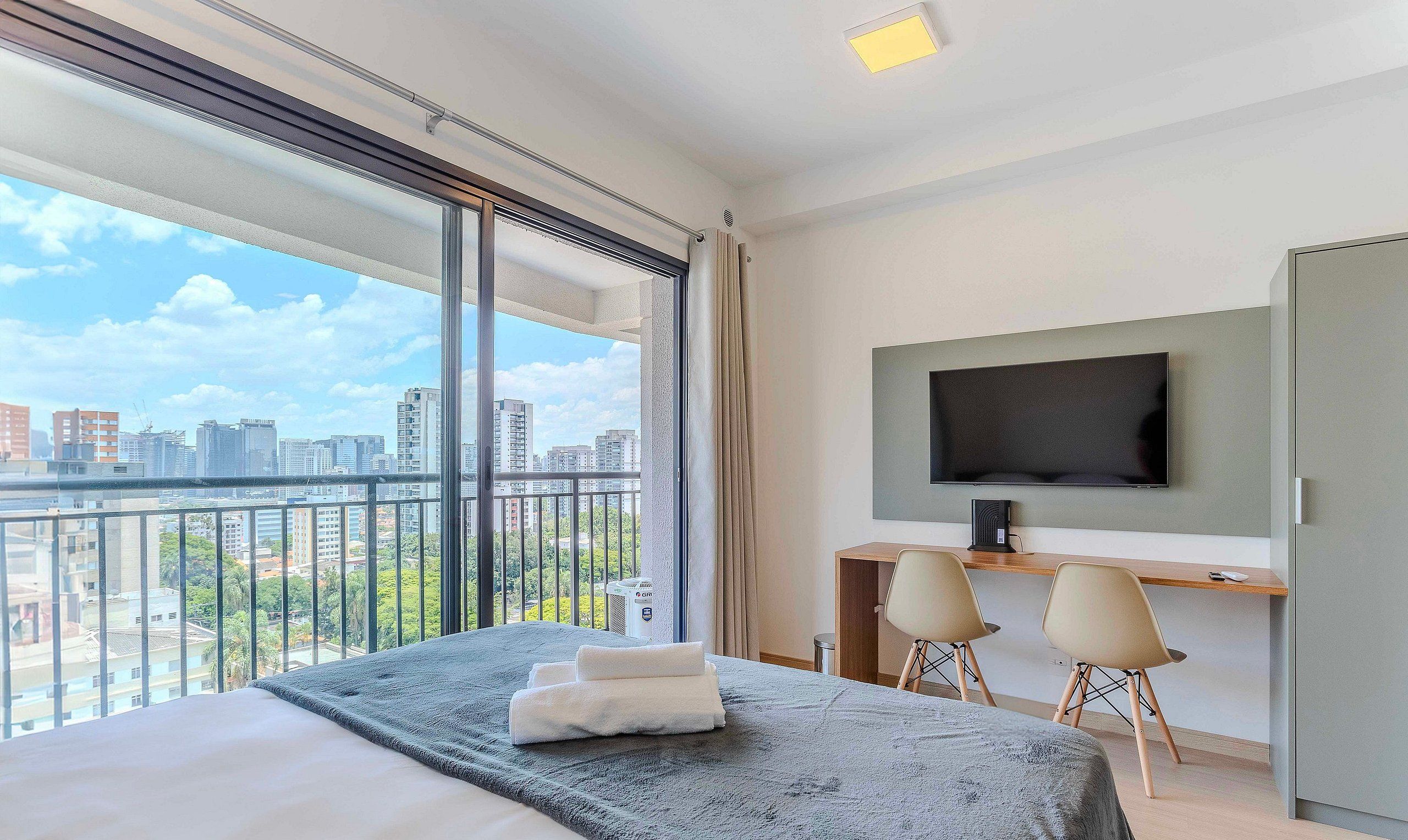 Ein Hotelzimmer mit einem großen Bett, einem Schreibtisch mit zwei Stühlen, einem Fernseher und Blick auf die Stadt.