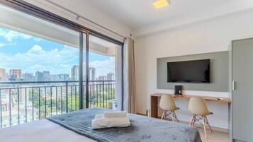 Ein Hotelzimmer mit einem großen Bett, einem Schreibtisch mit zwei Stühlen, einem Fernseher und Blick auf die Stadt.