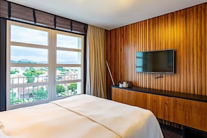 A hotel room with a bed, a TV mounted on a wooden wall, and a window with a view of buildings and greenery. - Renovated Penthouse in a Luxury Resort Ilc3503 (Florianópolis)