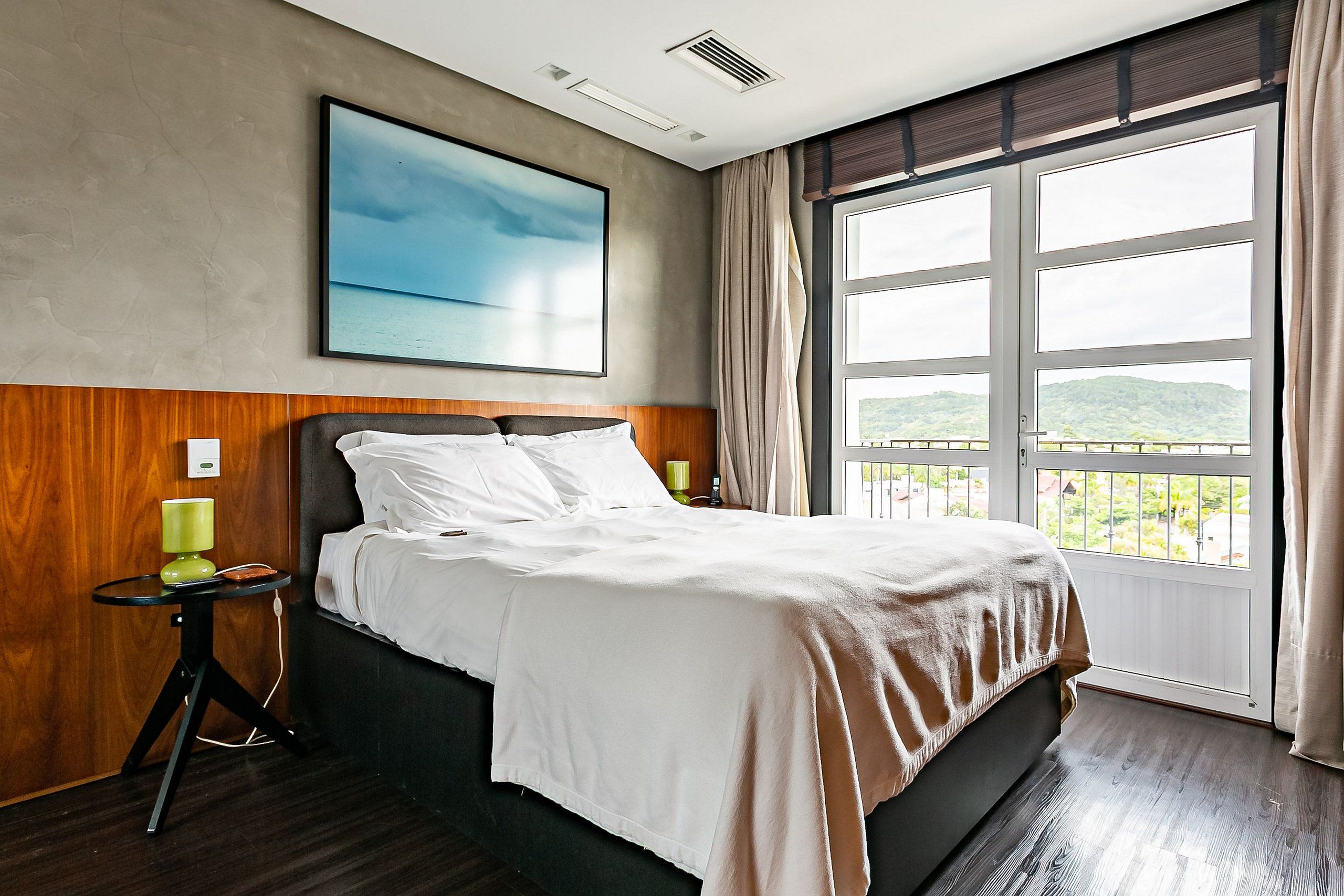 Quarto de hotel com uma cama grande, vista para o exterior e um quadro na parede.