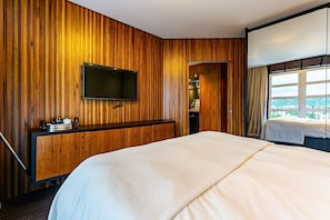 Une chambre d’hôtel avec un mur lambrissé en bois, un téléviseur à écran plat fixé au-dessus d’une commode en bois, un grand lit avec une literie blanche et une fenêtre avec des rideaux.