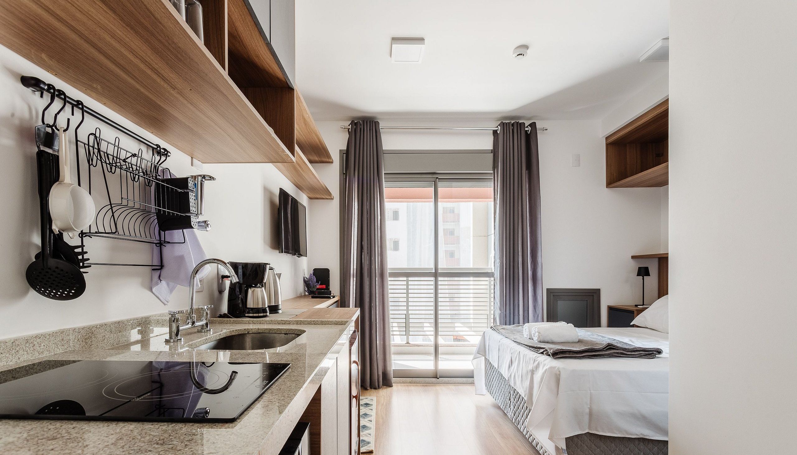 A modern hotel room with a kitchenette, a bed, and a view of the city.