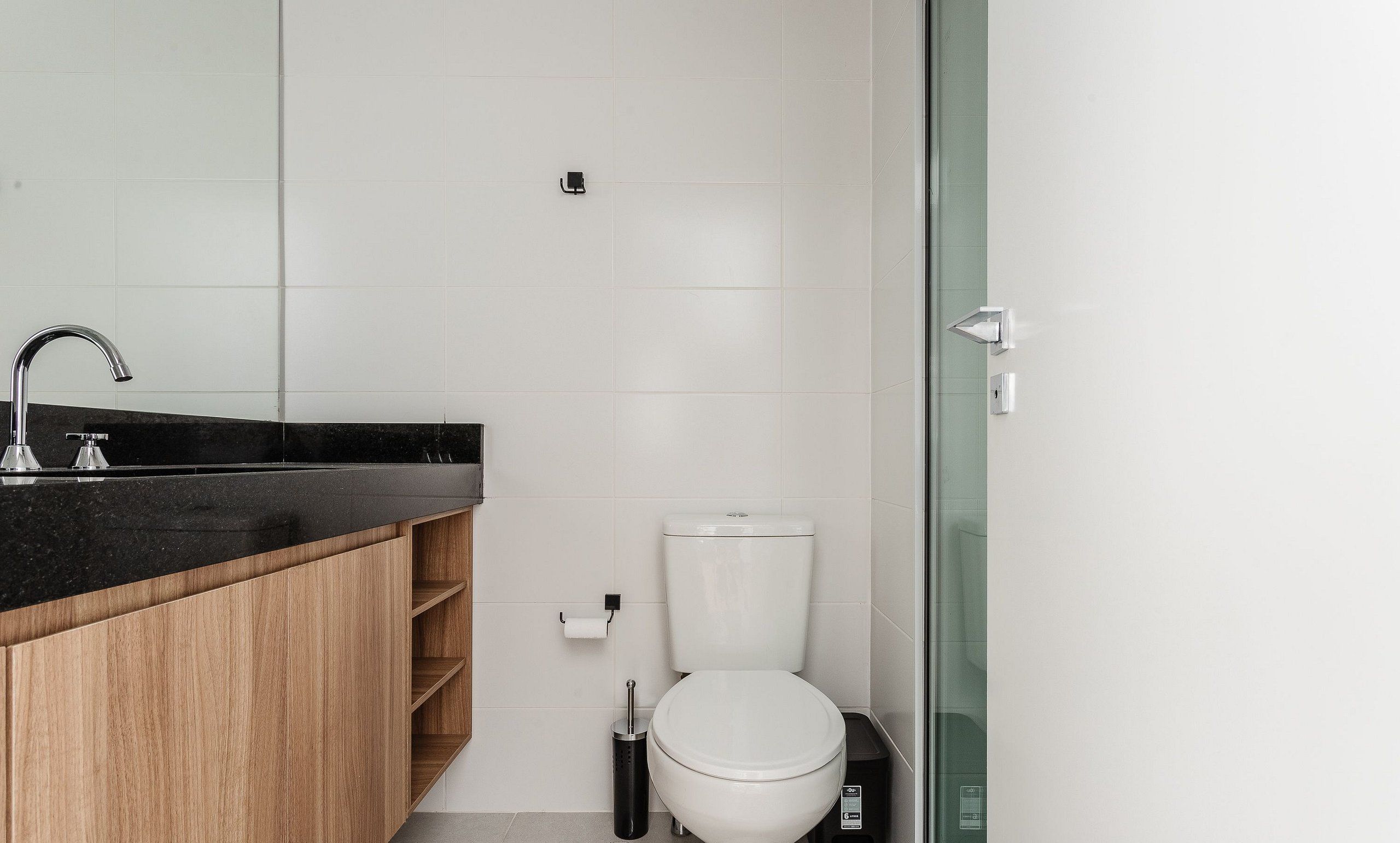 A modern bathroom with a black countertop, wooden cabinets, a white toilet, and a glass shower enclosure.