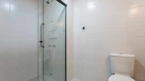 Et badeværelse med hvide fliser, et glasbadeværelse og et hvidt toilet.