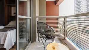 En balkon med en seng, en stol og udsigt over bybilledet.