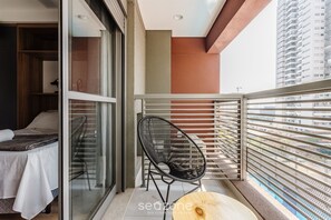 Uma varanda com cama, uma cadeira e vista para o horizonte urbano.