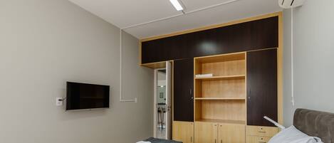 A bedroom with a bed, a TV mounted on the wall, and a wardrobe with open doors.