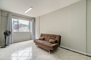A spacious room with a large window, a brown sofa, and a standing fan. - Comfortable Apart in the Center of Floripa Ejo0403 (Florianópolis)
