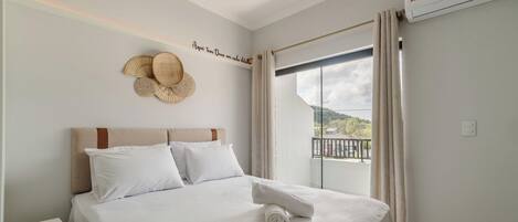 A hotel room with a bed, a wall-mounted decorative item, a window with curtains, and a view of the outdoors.