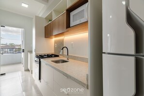 A modern kitchen with a stainless steel sink, a microwave, and a built-in oven. - Studio w/ BBQ Near the Airport - Rrc0206 (Florianópolis)