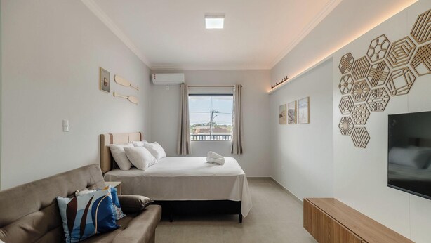 A modern bedroom with a bed, a sofa, a TV, and a window with a view. - Studio With Barbecue Near the Airport - Rrc0207 (Florianópolis)