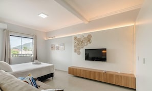 A modern hotel room with a bed, a sofa, a TV, and a wall art piece. - Studio With Barbecue Near the Airport - Rrc0207 (Florianópolis)