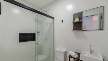 A modern bathroom with a glass-enclosed shower, a toilet, a sink, and a mirror with a shelf above it.