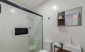Een moderne badkamer met een glazen douchecabine, een toilet, een wastafel en een spiegel met een plank erboven.