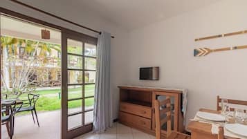 A room with a sliding glass door leading to a patio, a wooden desk with a television, and a dining area with a table set for two.