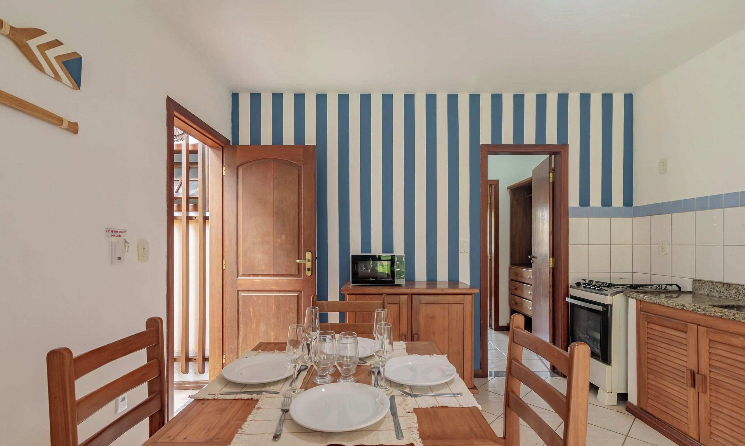 Un comedor con una mesa de madera dispuesta para cuatro, una cocina con microondas y una pared a rayas.