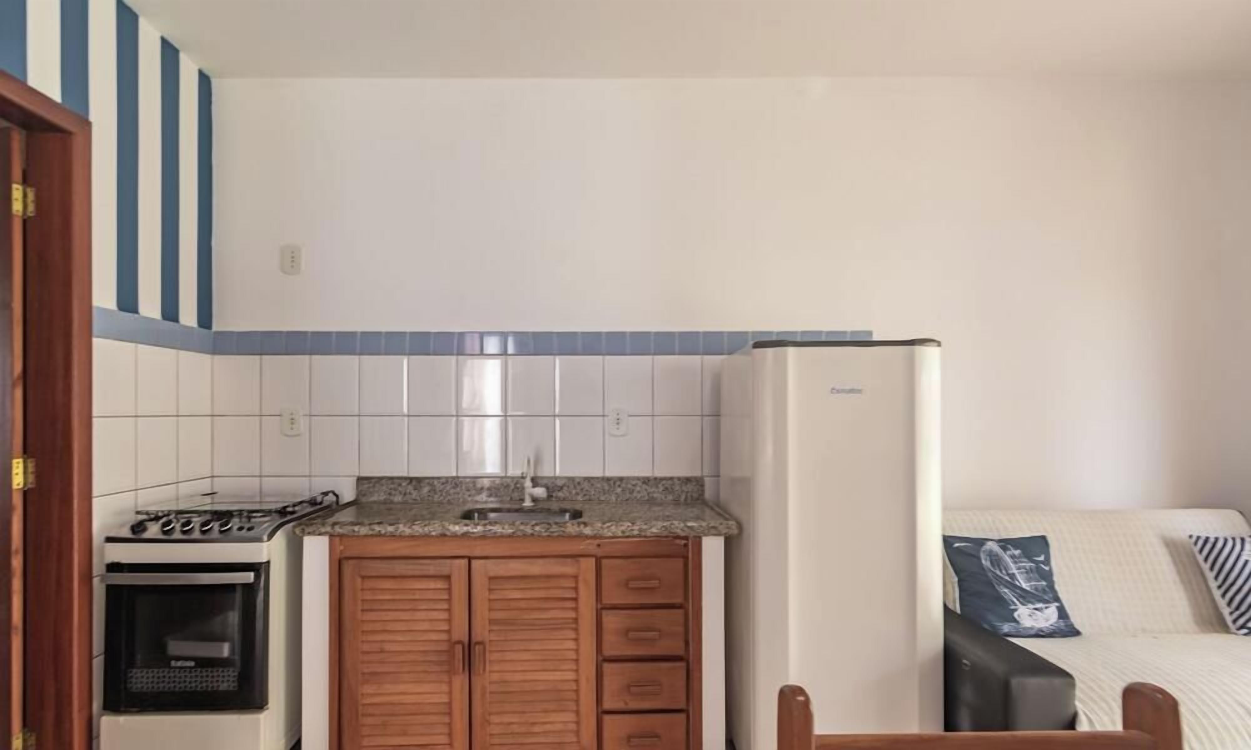 A compact kitchen with a stove, oven, and refrigerator, wooden cabinets, and a tiled backsplash.