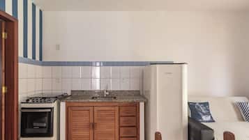 A compact kitchen with a stove, oven, and refrigerator, wooden cabinets, and a tiled backsplash.